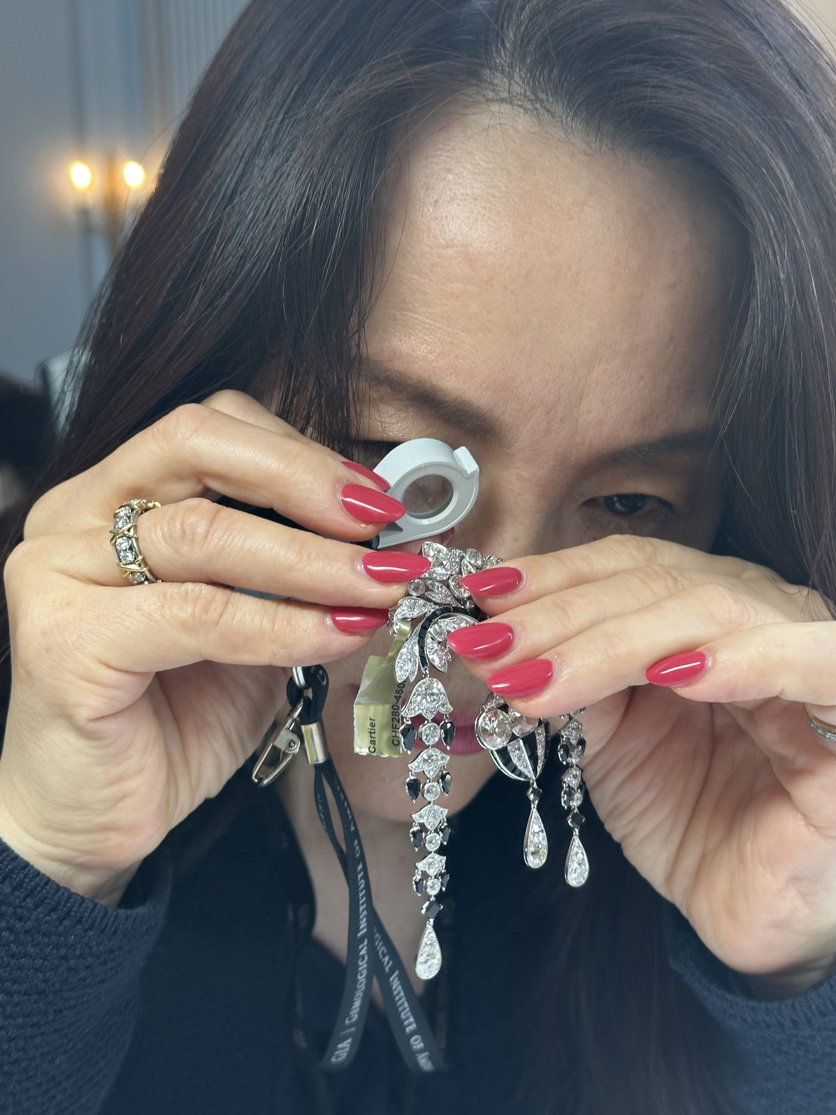 Close-up of Kehan Li examining a pair of long diamond pendant earrings down a loupe at the auction preview.